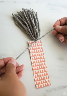 two hands are working on an ornament made from yarn and paper with scissors