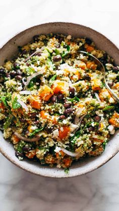 a bowl filled with rice and vegetables on top of a white countertop next to a spoon