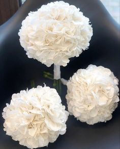 three white flowers sitting on top of a black chair