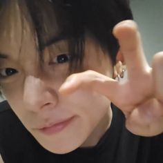 a woman making the v sign with her hand while wearing a black shirt and earrings