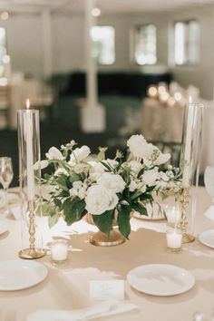 the centerpieces on this table are white roses and greenery in vases