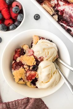 a bowl filled with ice cream and berries next to another bowl full of strawberries