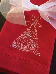 a red napkin with a white ribbon on it and a christmas tree embroidered on the front