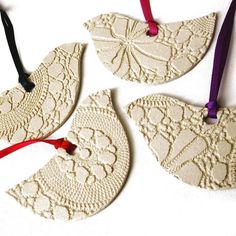 three pieces of lace hang from strings on a white surface with purple ribbon and red bow