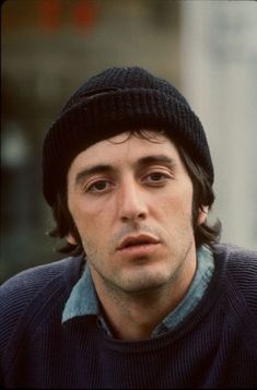 a man wearing a black hat and sweater looks off to the side with his eyes wide open