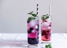 two glasses filled with drinks sitting on top of a white table covered in green leaves