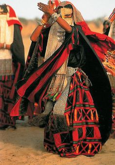 a group of people dressed in costumes and headdress walking through the desert with their hands together