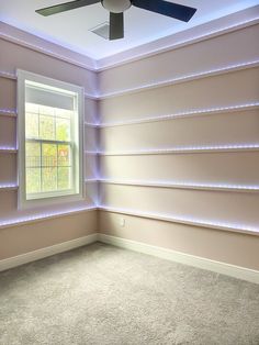 an empty room with a ceiling fan and some shelves on the wall behind it that are lit up