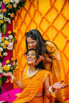 two women with face paint on their faces sitting in front of a yellow backdrop and flowers