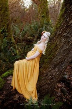 a woman in a yellow dress is leaning against a tree