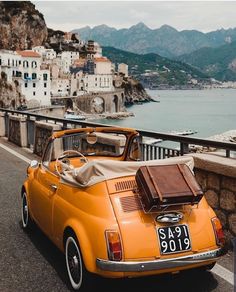 an orange car parked on the side of a road next to a body of water