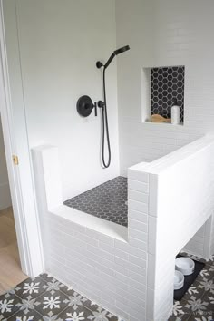 a white tiled bathroom with black and white floor tiles on the walls, shower head, and toilet seat