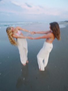 two beautiful women standing on top of a beach next to the ocean with their arms around each other