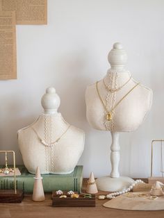 two white mannequins with pearls on them sitting next to each other in front of books