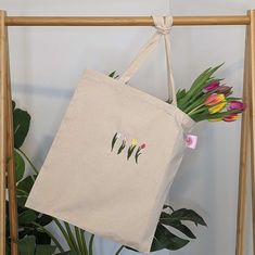 a tote bag with tulips on it hanging from a wooden frame next to a potted plant