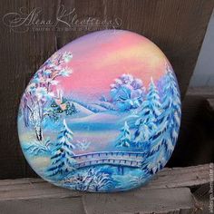 a painted rock sitting on top of a wooden fence next to a tree filled with snow