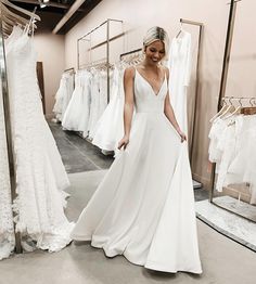 a woman standing in front of a rack of wedding dresses