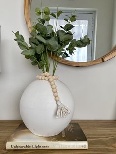 a white vase filled with green plants on top of a wooden table next to a mirror