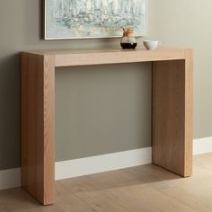 a wooden table with a painting on the wall above it and a cup in front of it