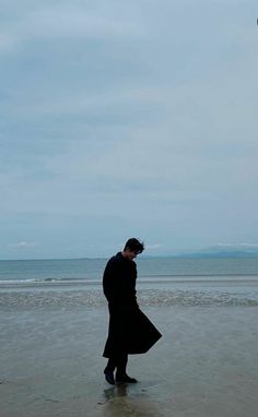 a man standing on top of a sandy beach under a kite flying in the sky