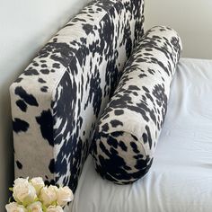 a black and white pillow sitting on top of a bed next to a vase with flowers