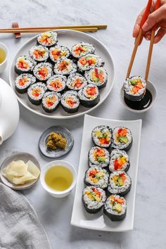 sushi on plates with chopsticks and dipping sauce next to each other,