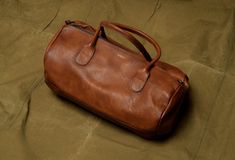 Our leather Gym Bag has the cylindrical shape of vintage sports bags. Handcrafted in full-grain leather, lined in canvas on the inside with a zipped storage pocket, its modern and retro look at the same time gives it an elegant style. It can easily be stored in a locker room, it's an ideal bag to go to a boxing or training session. - Full grain leather - Length : 45 cm - Width : 26 cm - Height : 26 cm - Weight : 1,2 kg - Zipped interior storage pocket - Adjustable strap Vintage Soft Leather Duffle Bag For Daily Use, Vintage Leather Duffle Bag With Soft Leather, Vintage Leather-lined Satchel Duffle Bag, Vintage Business Duffle Bag With Leather Handles, Vintage Duffle Bag With Leather Handles For Business, Vintage Soft Leather Duffle Bag, Vintage Soft Leather Everyday Travel Bag, Vintage Soft Leather Travel Bag For Everyday, Classic Soft Leather Duffle Bag In Cognac