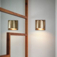 two lights on the side of a white wall next to a mirror and wooden door