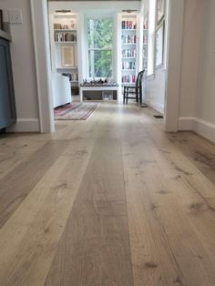 an empty hallway with wood floors and white walls, leading to a living room area