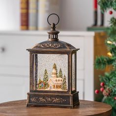 a small christmas lantern sitting on top of a wooden table next to a christmas tree