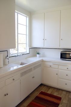 a kitchen with white cabinets and wood flooring next to a microwave on top of a counter