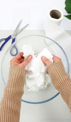 two hands holding tissue on top of a glass plate next to scissors and paper towels