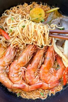 noodles and shrimp are being cooked in a wok with chopsticks on the side