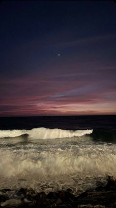 the sky is purple and pink as it sets over the ocean with waves crashing in to shore