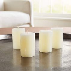 three white candles sitting on top of a metal table next to a couch and window