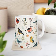 a white mug with birds on it sitting next to some lemons