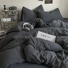 an unmade bed with grey sheets and pillows