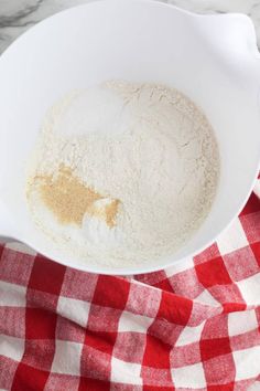 a white bowl filled with flour on top of a red and white checkered table cloth