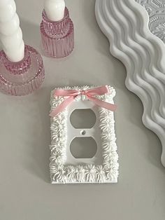 a decorative light switch cover with a pink bow on the front and two white candles in the back