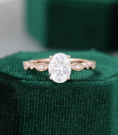 a diamond ring sitting on top of a green velvet cushioned box with the engagement ring in it's center