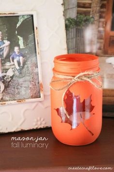 an orange mason jar sitting on top of a wooden table next to a framed photo