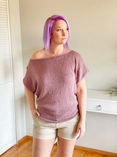 a woman with purple hair is standing in front of a wall and looking off to the side