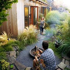 two people sitting around a fire pit in the middle of a garden with plants and rocks