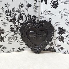 a heart shaped metal object sitting on top of a white table next to a floral wallpaper