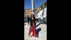 a woman standing in front of a waterfall with her arms around her waist and wearing sunglasses