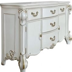 an ornate white dresser with gold trimmings on the doors and drawers, is shown