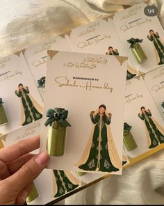 a person holding up some cards with green dresses on them and gold trimmings