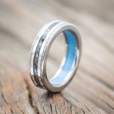 a wedding ring with blue and white inlays sits on a piece of wood