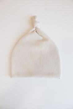 a white knitted hat with a knot on the front and side, against a white background