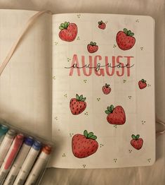 an open notebook with strawberries and the words august written on it next to crayons